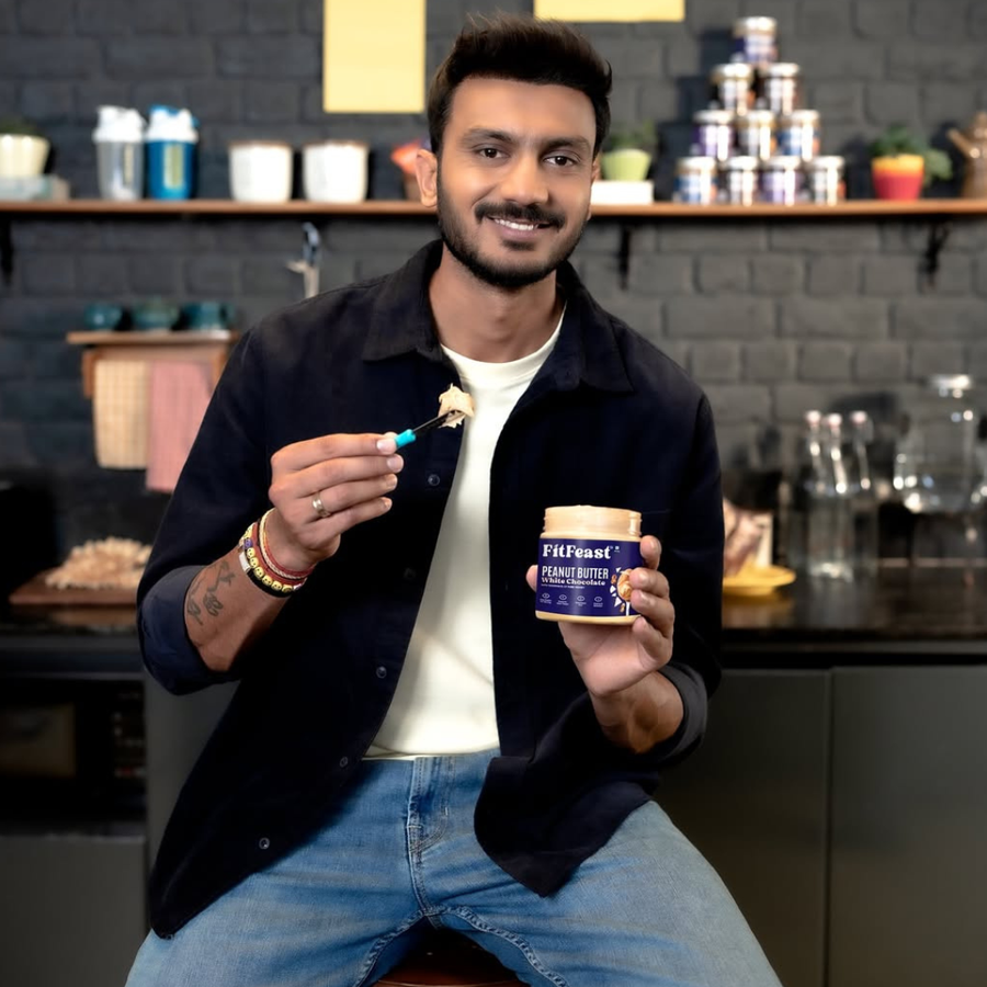 Man holding a container of FitF觉 peanut butter in a kitchen setting