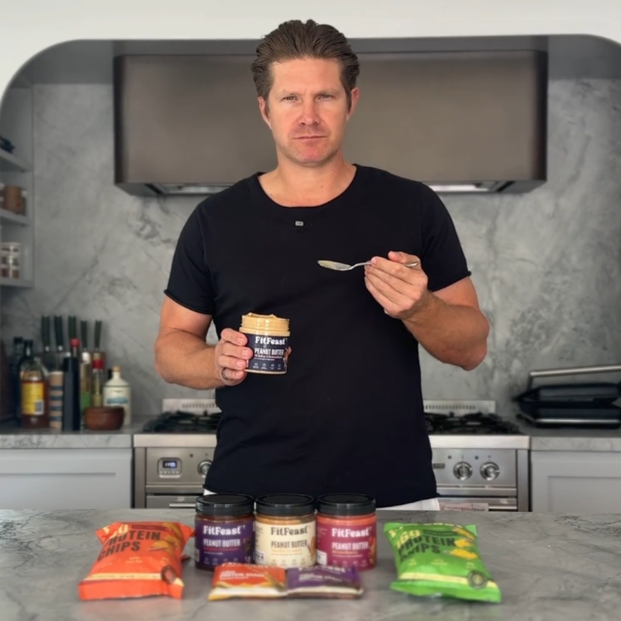 Man holding a jar and spoon in a kitchen with various food products on the counter